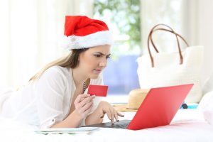 Confused woman paying online on christmas holidays lying on a bed in an hotel room