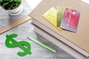 dollar sign and credit cards for fee-paying education on gray student desk background